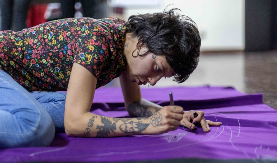 Mujer joven dibuja sobre una bandera morada. Foto: Laura Imery / Idartes.