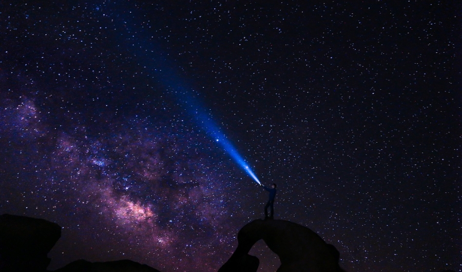 Cielo estrellado con señor apuntando al cielo con linterna. 