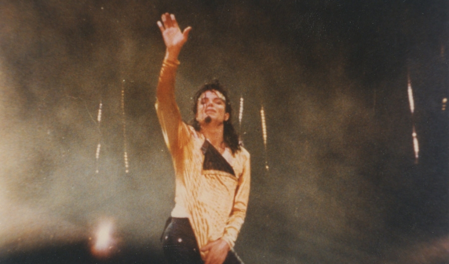 Michael Jackson parado levantando la mano en concierto.