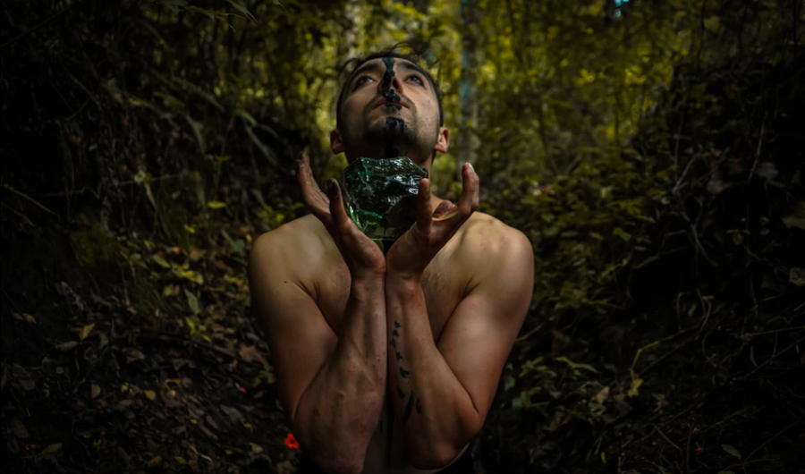 hombre sosteniendo una roca verde con sus manos con una selva de fondo.
