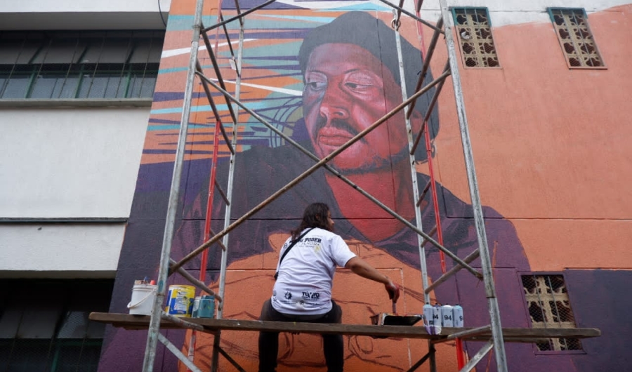 Persona pinta un gran mural de día.