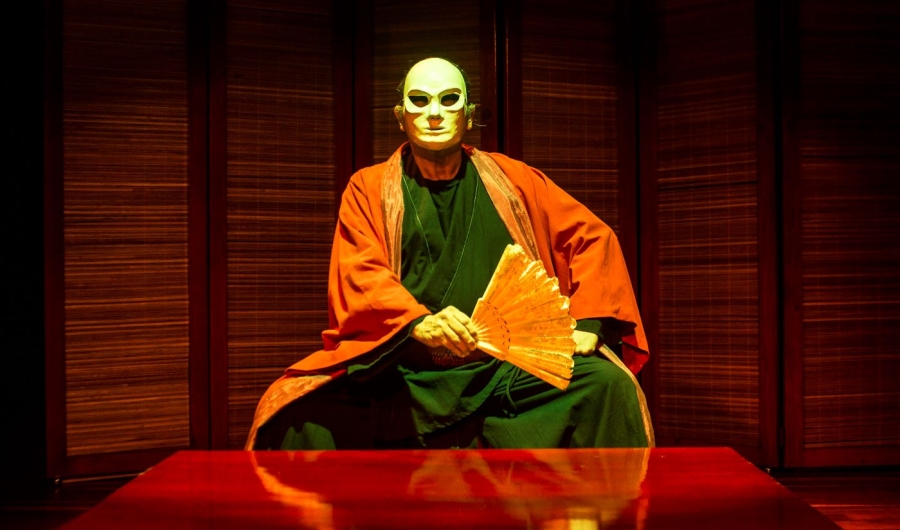Hombre con una máscara y un kimono sentado en la tarima del escenario