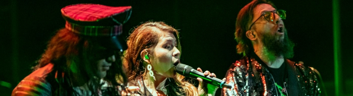 Una mujer cantando y dos hombres a su lado tocando guitarra