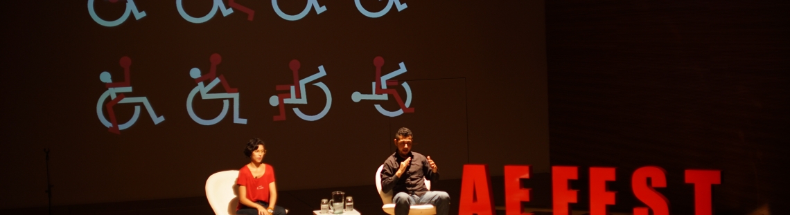 Conversatorio entre dos personas con proyección de sillas de ruedas ilustradas de fondo. 