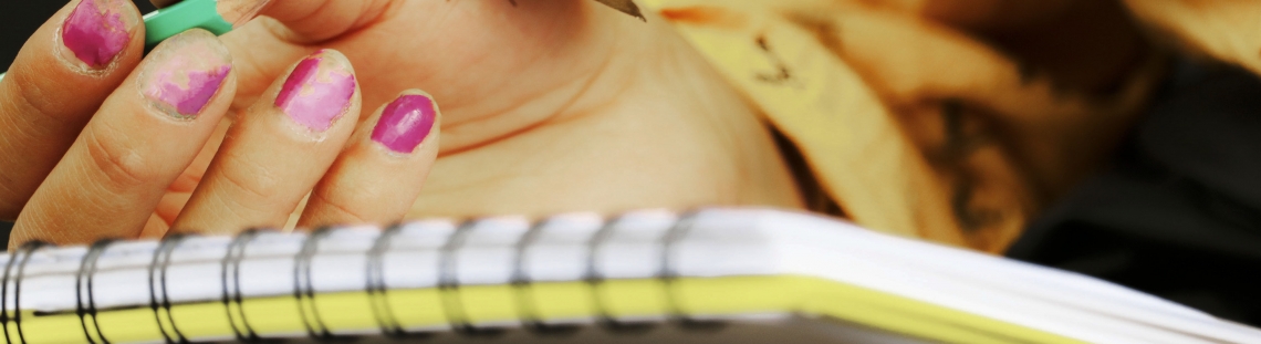 Foto de una mano que sujeta un lápiz con una mariposa que se posa en su dorso sobre una libreta