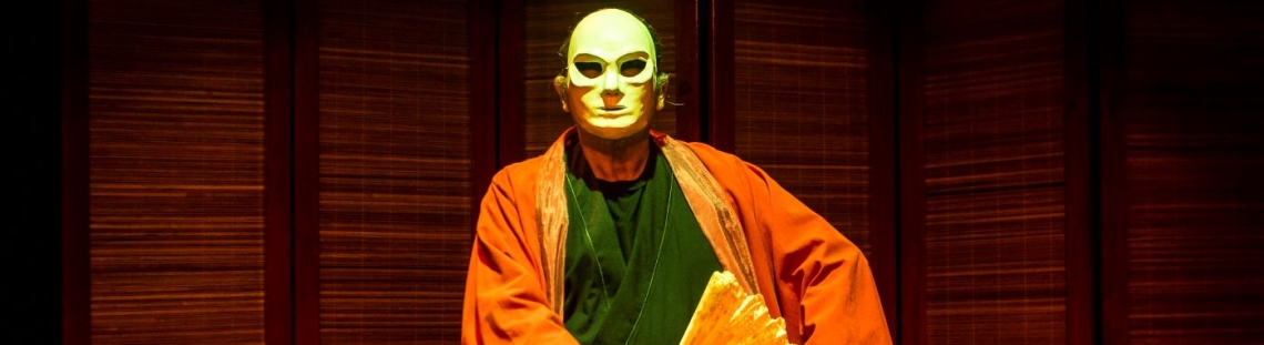 Hombre con una máscara y un kimono sentado en la tarima del escenario 