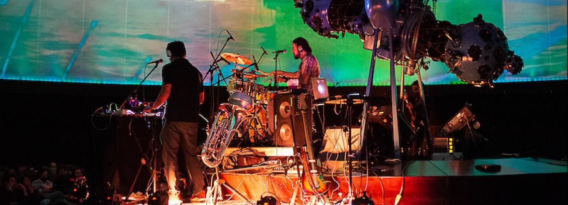 Agrupación musical tocando en vivo en tarima del domo del Planetario de Bogotá con proyección audiovisual. 