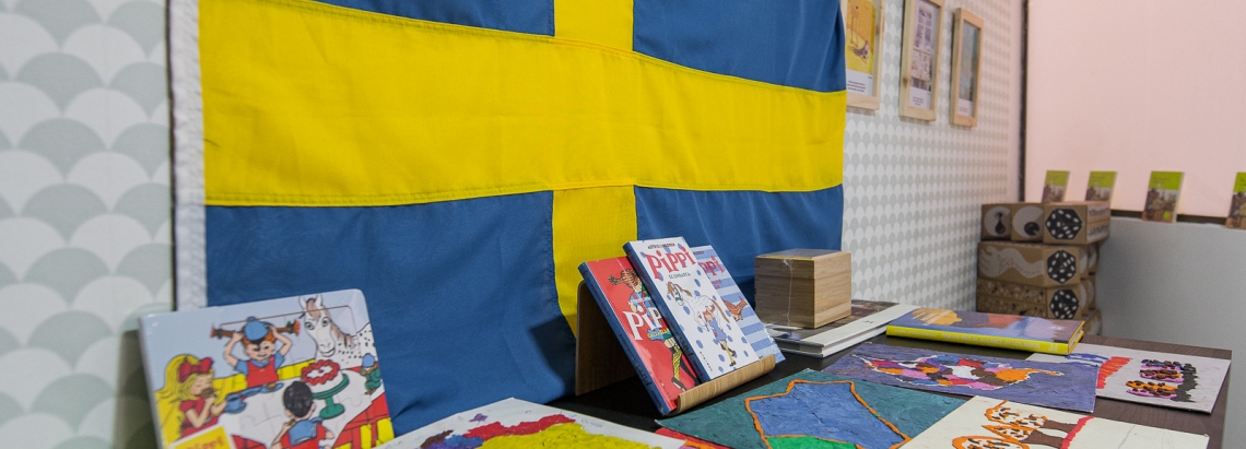 Mesa con libros de Pippi Calzaslargas y obras de arte hechas por niños, en el fondo la bandera de Suecia