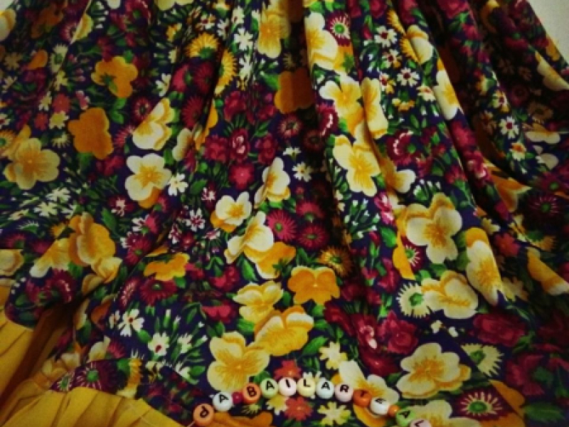 Falda de flores con las letras de la obra en un collar de cuadritos