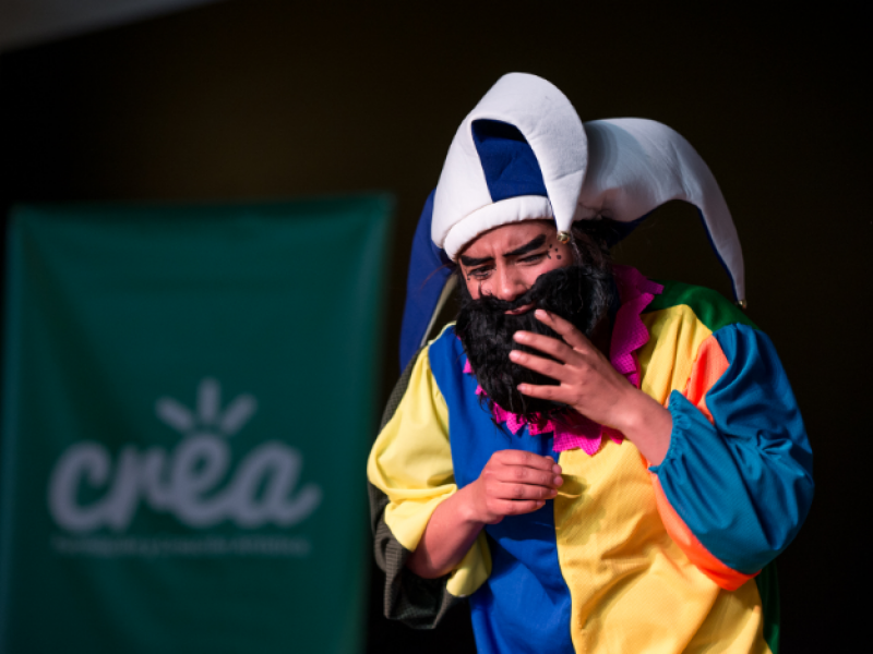 Hombre actuando vestido con traje de colores, gorro y barba negra