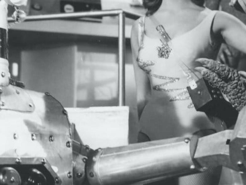 Escena cinematográfica de ciencia ficción en blanco y negro. Un robot, un dinosaurio y una persona. 