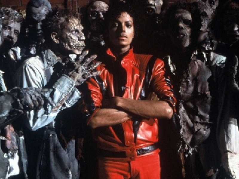 Michael Jackson en traje rojo entre varios zombies en famoso video de Thriller. 