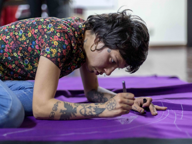 Mujer joven dibuja sobre una bandera morada. Foto: Laura Imery / Idartes.