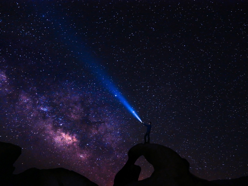 Cielo estrellado con señor apuntando al cielo con linterna. 