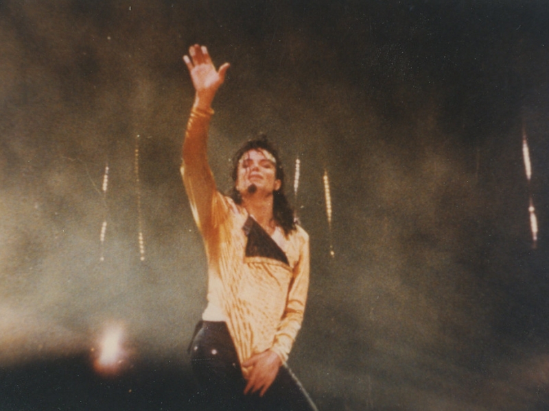 Michael Jackson parado levantando la mano en concierto. 