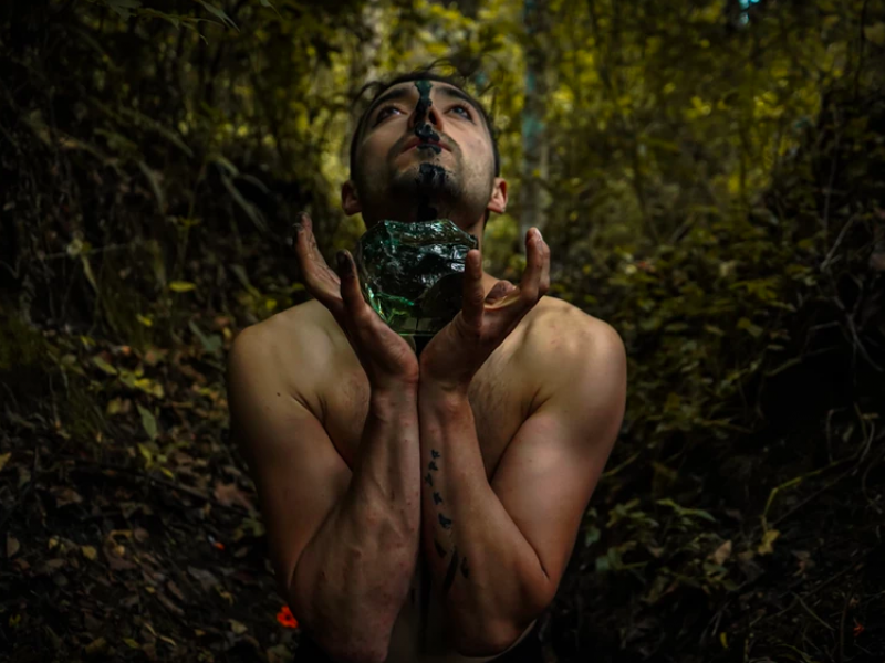 hombre sosteniendo una roca verde con sus manos con una selva de fondo. 