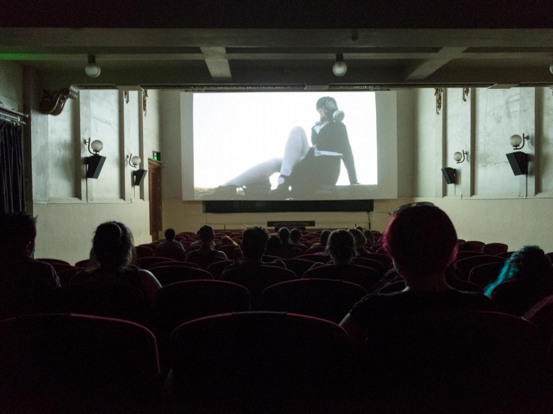 Personas en una sala de cine con una proyección de una mujer en blanco y negro. 