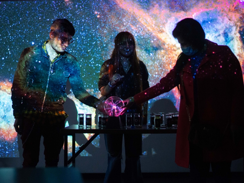 Tres personas interactuando con una bola de luz y una proyección del espacio atrás. 