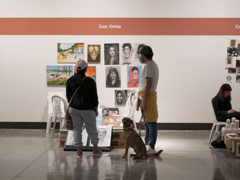 Dos personas y un perro admiran las obras en un stand de las Ferias Locales de Artes en La Candelaria