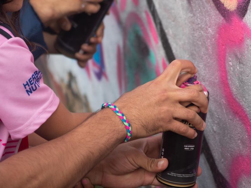 Plano cerrado de alguien utilizando una lata de pintura rosada en arte urbano para MAB