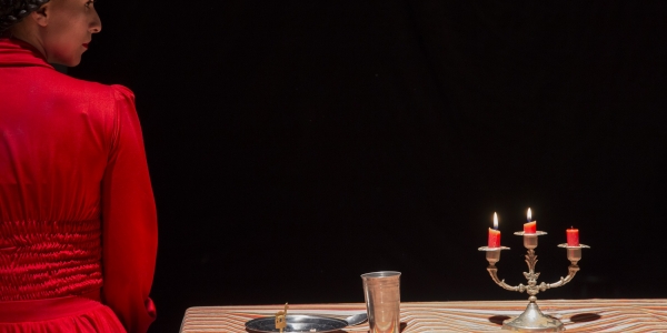 Mujer vestida de rojo al lado de una mesa con plato, vaso y velas.