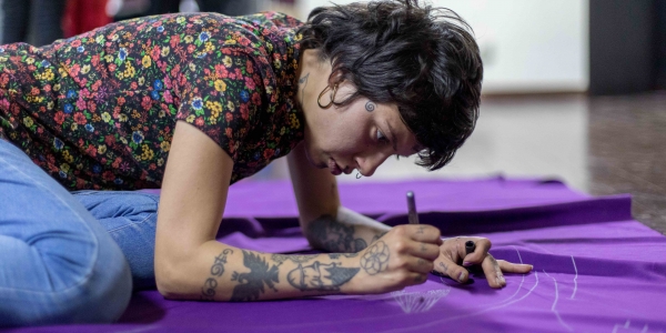 Mujer joven dibuja sobre una bandera morada. Foto: Laura Imery / Idartes.