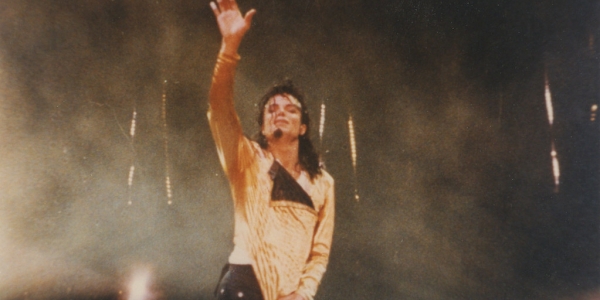 Michael Jackson parado levantando la mano en concierto. 