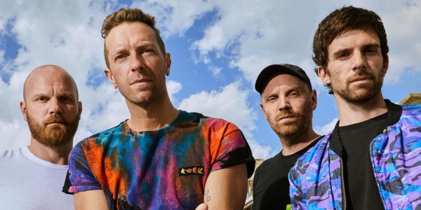 Integrantes de Coldplay con cielo azul y nubes de fondo. 