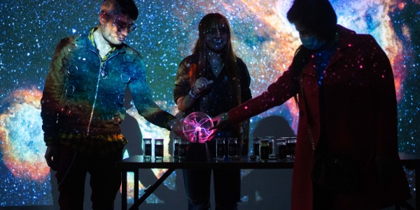 Tres personas interactuando con una bola de luz y una proyección del espacio atrás. 