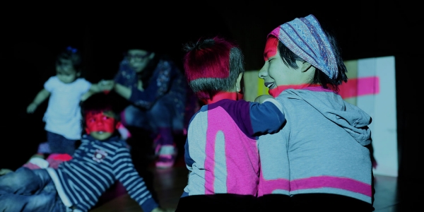 Niños en un cuarto oscuro alumbrados por luces de colores. 