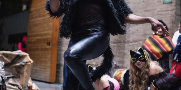 Mujer trans vestida en cuero simulando una gata de noche en interior.