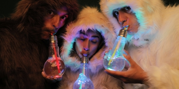Tres artistas con trajes completos de peluche beben agua de unos bombillos a través de pitillos