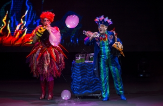 Actriz y actor haciendo burbujas sobre un escenario colorido