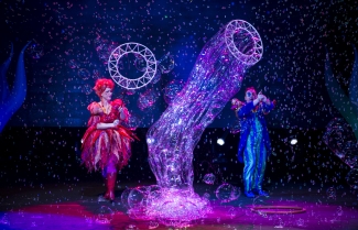 Hombre vestido de azul y mujer vestida de rosa en escenario con muchas burbujas