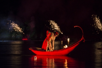 Góndola roja con actriz sobre el lago y juegos pirotécnicos