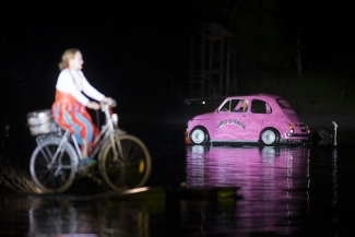 Auto fucsia y actriz en bicicleta sobre el lago.