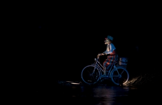 Actor sobre el lago en bicicleta con traje de colores.
