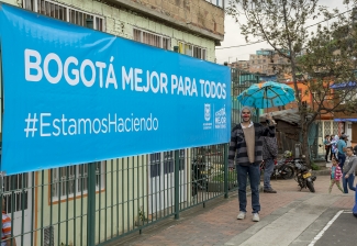 Hombre disfrazado y con sombrilla frente a anuncio de Bogotá Mejor para Todos.