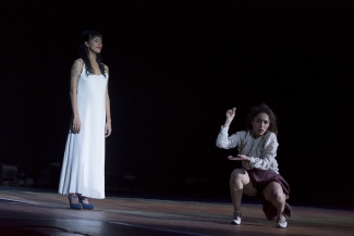 Dos  mujeres, una de rodillas y otra de  pie en el escenario