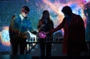 Tres personas interactuando con una bola de luz y una proyección del espacio atrás. 