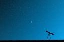 Cielo azul con estrellas y un telescopio en el suelo. 