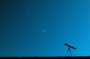Cielo azul con estrellas y un telescopio en el suelo. 